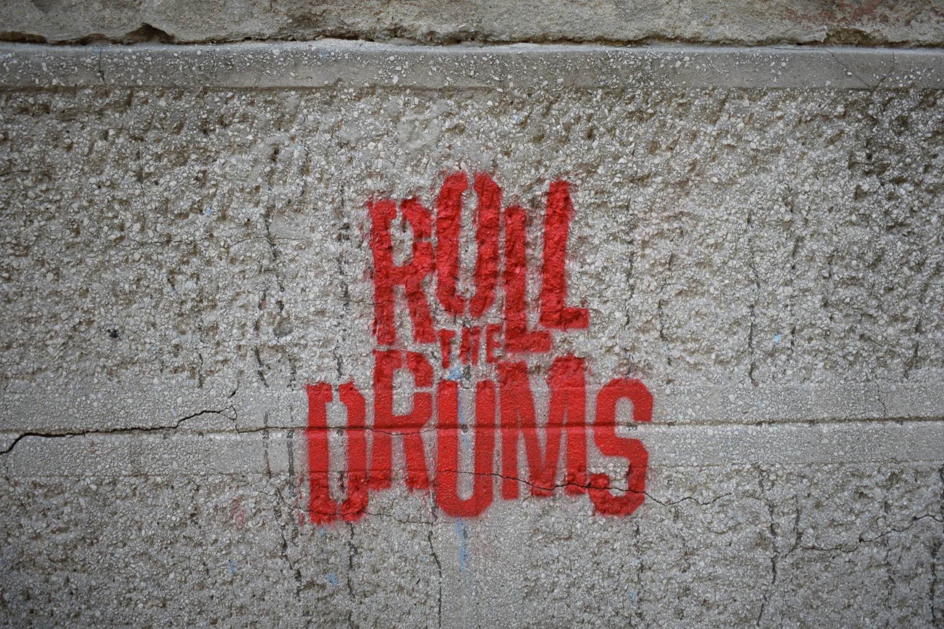 Pintada en rojo con las palabras «Roll the drums» sobre una pared de hormigón gris